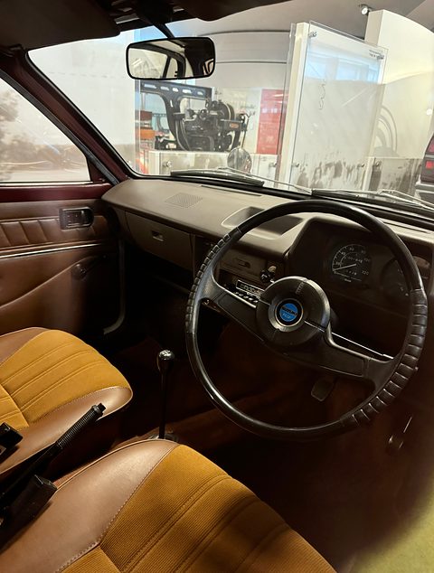 Through an open door: a two-spoke steering wheel, a brown dashboard and tan seats. Opens a larger view