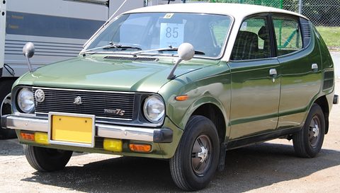 Green small hatchback-shaped car with a white roof, black grille and a yellow plate. Opens a larger view