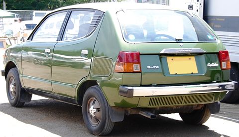 Rear three-quarter of a green small car with a ribbed side vent and an ALTO-style plate area. Opens a larger view