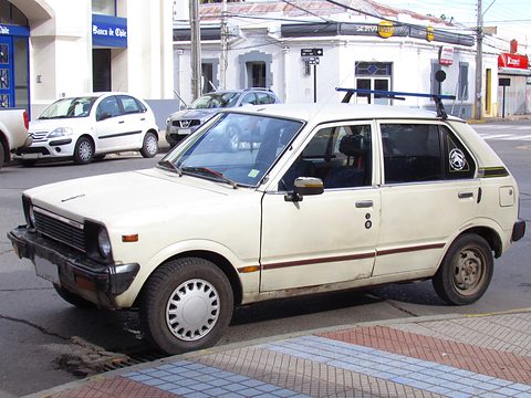 Cream small five-door car parked at a kerb on a sunny street corner. Opens a larger view