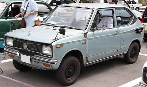 Pale blue small saloon with a black grille and square headlamps, a woman and child at left. Opens a larger view