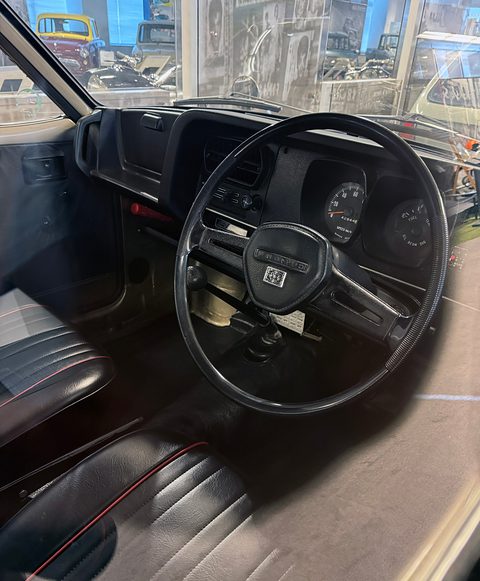 Through an open door: a black two-spoke wheel, a dark dashboard and black seats. Opens a larger view
