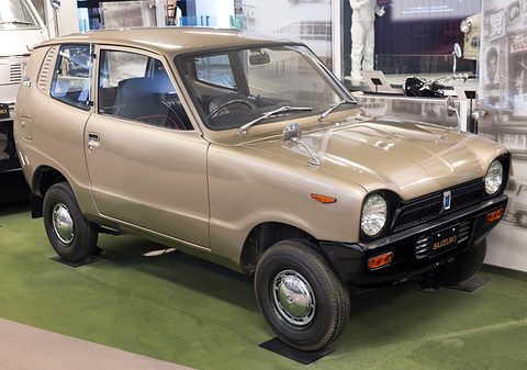 Gold small van-like car on green carpet, display photographs behind. Opens a larger view