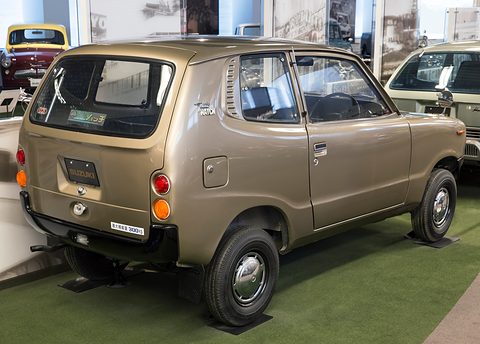Rear three-quarter of a gold small van-like car with a side-hinged tailgate, on green carpet. Opens a larger view
