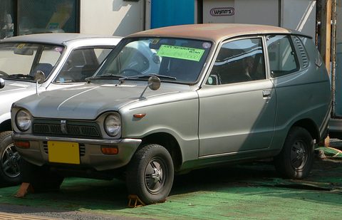 Silver small van-like car with a rusty roof, a green sign in its windscreen, in a garage forecourt. Opens a larger view