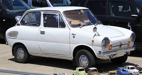 Side view of a white rounded small saloon with cooling slots behind the rear window, toy cars on the ground. Opens a larger view