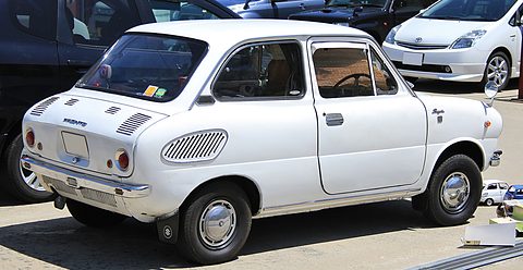 Rear three-quarter of a white small saloon with oval slotted grilles on the rear flanks.