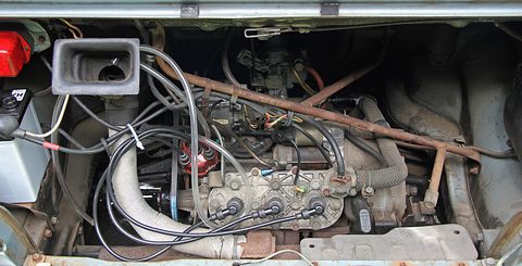 Rear engine bay with a small three-cylinder engine, black ignition leads, a silver hose and a rubber air intake. Opens a larger view