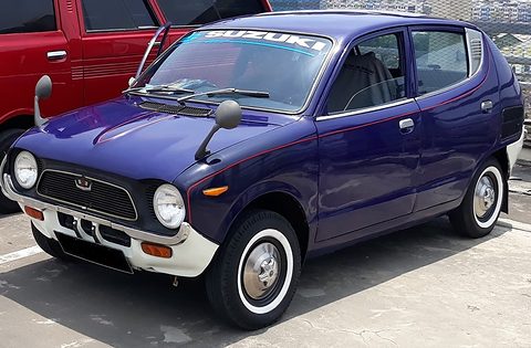 Dark blue four-door small car with whitewall tyres and a Suzuki sticker on the windscreen. Opens a larger view