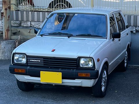 White small five-door car with a black grille and a yellow plate, in front of a fence. Opens a larger view