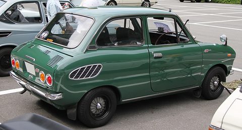 Rear three-quarter of a dark green small saloon with oval slotted vents and twin tail lamps. Opens a larger view