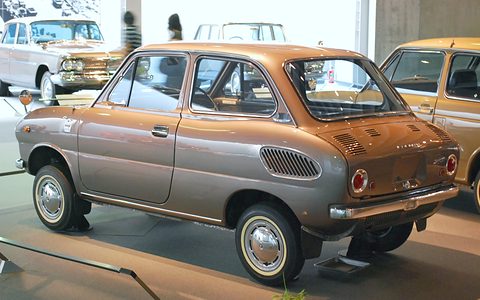 Rear three-quarter of a bronze small saloon with slotted rear vents, other cars around it. Opens a larger view