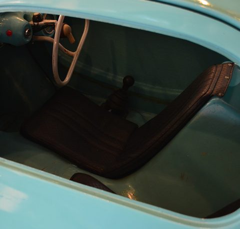 Black vinyl seat, a white steering wheel with a flattened rim and a floor gear lever inside a turquoise shell.