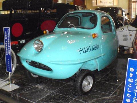 Turquoise teardrop-shaped three-wheeler with FUJICABIN painted on the side, one headlamp and a small front wheel. Opens a larger view