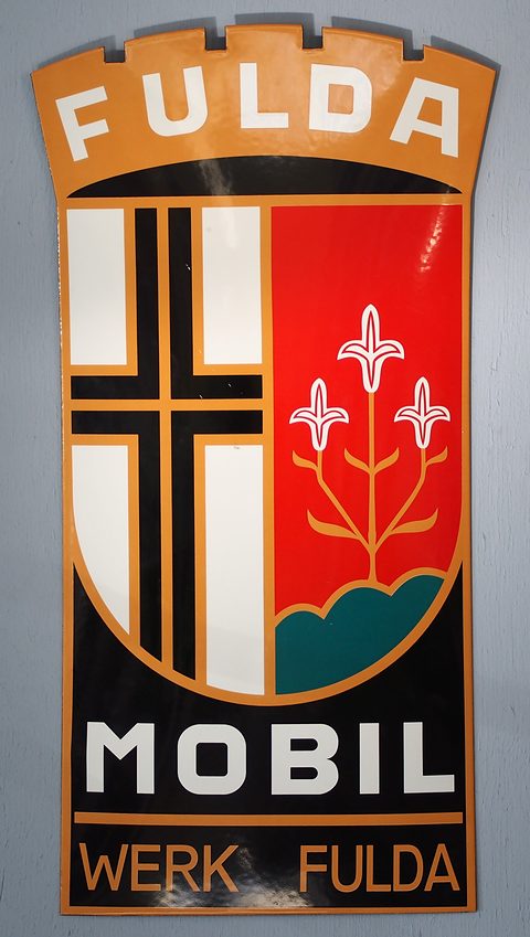 Tall enamel sign with the Fulda crest, a black cross and three white lilies, above the words MOBIL and WERK FULDA. Opens a larger view