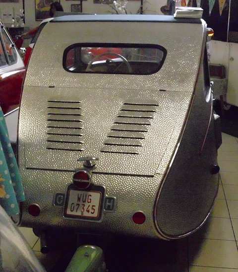 Back of a hammered-aluminium three-wheeler with angled louvres, a small rear window and a German number plate. Opens a larger view