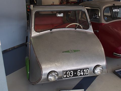 Dimpled silver three-wheeler facing the camera, green wheel arch, two headlamps and plate FW 03-6410. Opens a larger view