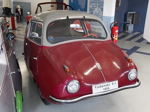 Two-tone red and grey rounded three-wheeler with a “Fuldamobil S-2 1955” display plate in a museum hall.