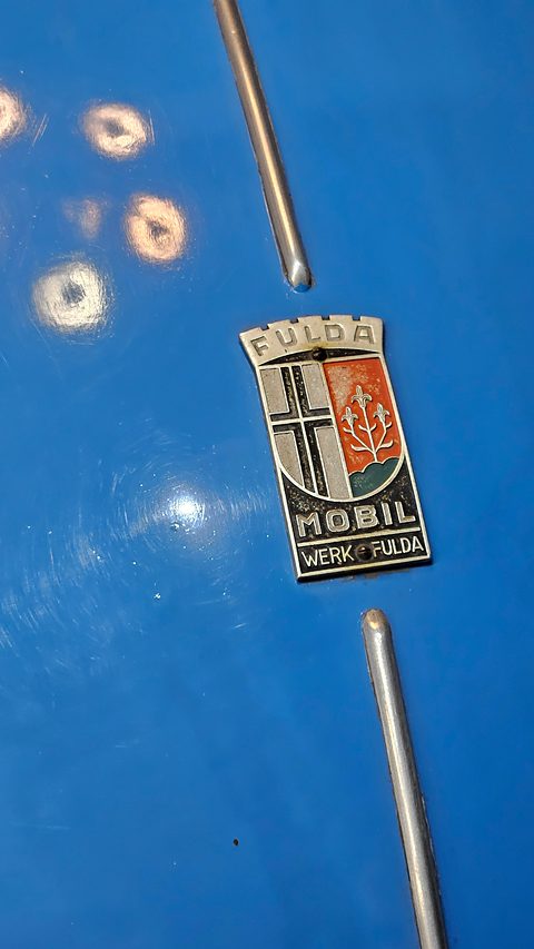 Enamel Fulda Mobil “Werk Fulda” shield badge between two chrome strips on blue paint. Opens a larger view