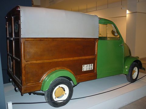 Rear quarter of a small van with a dark varnished wooden box, a grey canvas top and a green cab. Opens a larger view