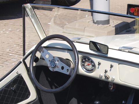 Cream painted dashboard with a black three-spoke steering wheel, one round dial, toggle switches and a mirror on the scuttle. Opens a larger view