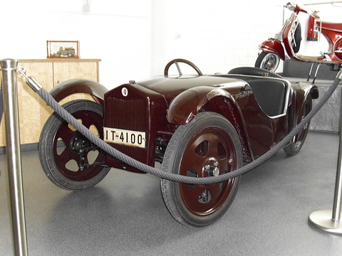 Maroon open two-seater with a flat radiator grille and plate IT-4100, seen from the front left behind a rope. Opens a larger view