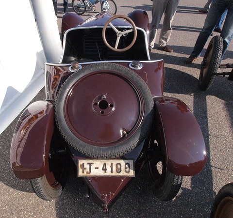Rear of a maroon open car with a spare wheel on its pointed tail, plate IT-4100 and the steering wheel visible. Opens a larger view