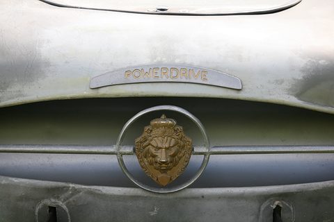 Close view of a script nameplate reading Powerdrive above a gold lion’s head on weathered grey paint. Opens a larger view