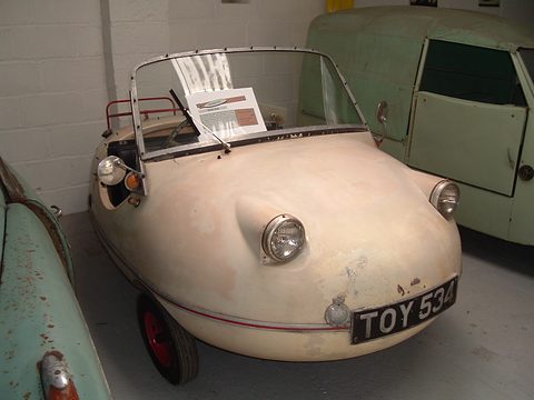 Weathered cream bubble-shaped three-wheeler with a small windscreen and an information sheet on it.