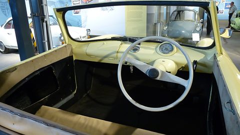 Cream dashboard with a white two-spoke wheel inside a yellow open body, a white car outside.