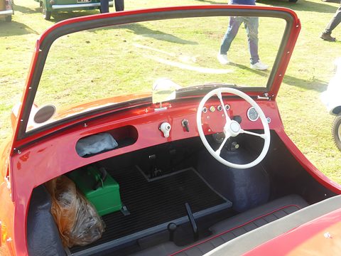 Looking into a red open cockpit at a white steering wheel and a row of round dials. Opens a larger view