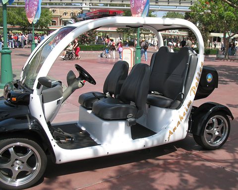 Black and white open four-seat electric car with a light bar and gold lettering on a red-paved street. Opens a larger view