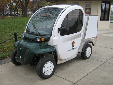 White and dark green electric utility vehicle with a Park Ranger door badge and rear box on a path. Opens a larger view