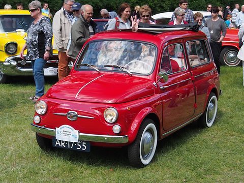 Red small estate car with white-wall tyres on grass, visitors standing behind it. Opens a larger view