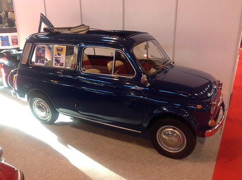 Dark blue small estate car with an open fabric roof on a brightly lit show stand. Opens a larger view