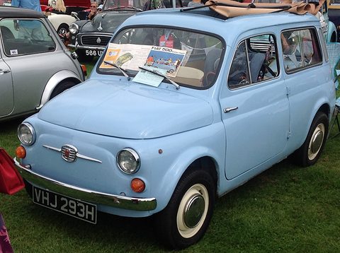 Light blue small estate with its canvas roof open and brochures on the windscreen, parked on grass among cars. Opens a larger view