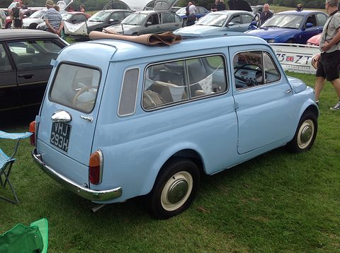 Rear of a pale blue small estate car with the fabric roof folded open, on grass among other cars. Opens a larger view