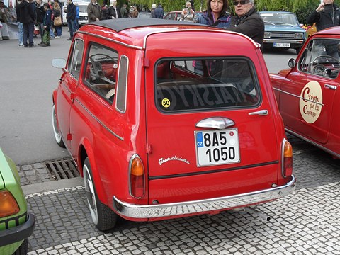 Rear of a red small estate car with a script badge, number plate and side-hinged rear door. Opens a larger view
