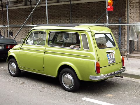 Rear of a lime-green small estate car with pillar air grilles, parked by scaffolding on a street. Opens a larger view