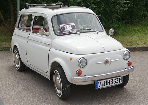 White small estate car with chrome bumpers parked on tarmac before a green bank. Opens a larger view