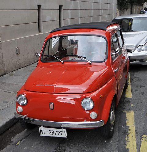 Front of an orange small estate car parked on a narrow street beside a stone wall. Opens a larger view