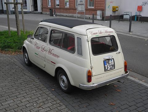 Cream small estate from the rear left with lettering on its side and rear door, parked in a car park. Opens a larger view