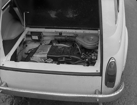 Looking down into the open tail of a small car at a flat engine with its air cleaner, beneath a load floor. Opens a larger view