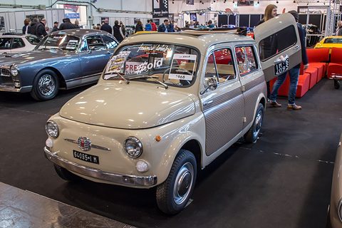Beige small estate car on a show stand with its rear door open, other classics behind. Opens a larger view