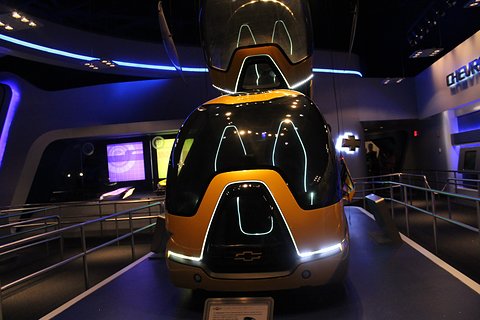 Orange and black egg-shaped two-wheeled pod with a Chevrolet bowtie under blue display lighting.