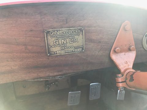 A brass plate reading G.N. Cyclecar, G.N. Ltd, Elms Works, Hendon, England, with engine and chassis numbers, on wood.