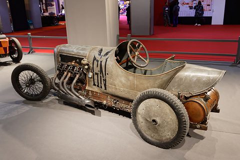 A weathered unpainted racing car with an exposed engine and exhaust pipes, GN lettered on its side. Opens a larger view