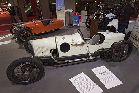 Side view of a white single-seat racing car with a round port in its flank, information sheets on the floor. Opens a larger view