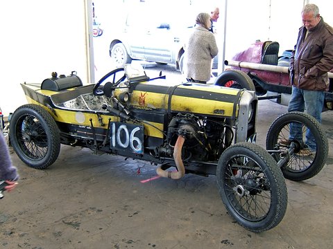 A yellow and black racing special numbered 106 on concrete, two people standing beside it. Opens a larger view