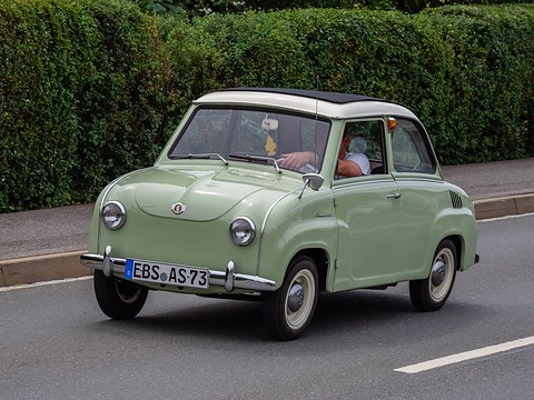 Pale green saloon driving on a road beside a hedge, a driver visible inside. Opens a larger view